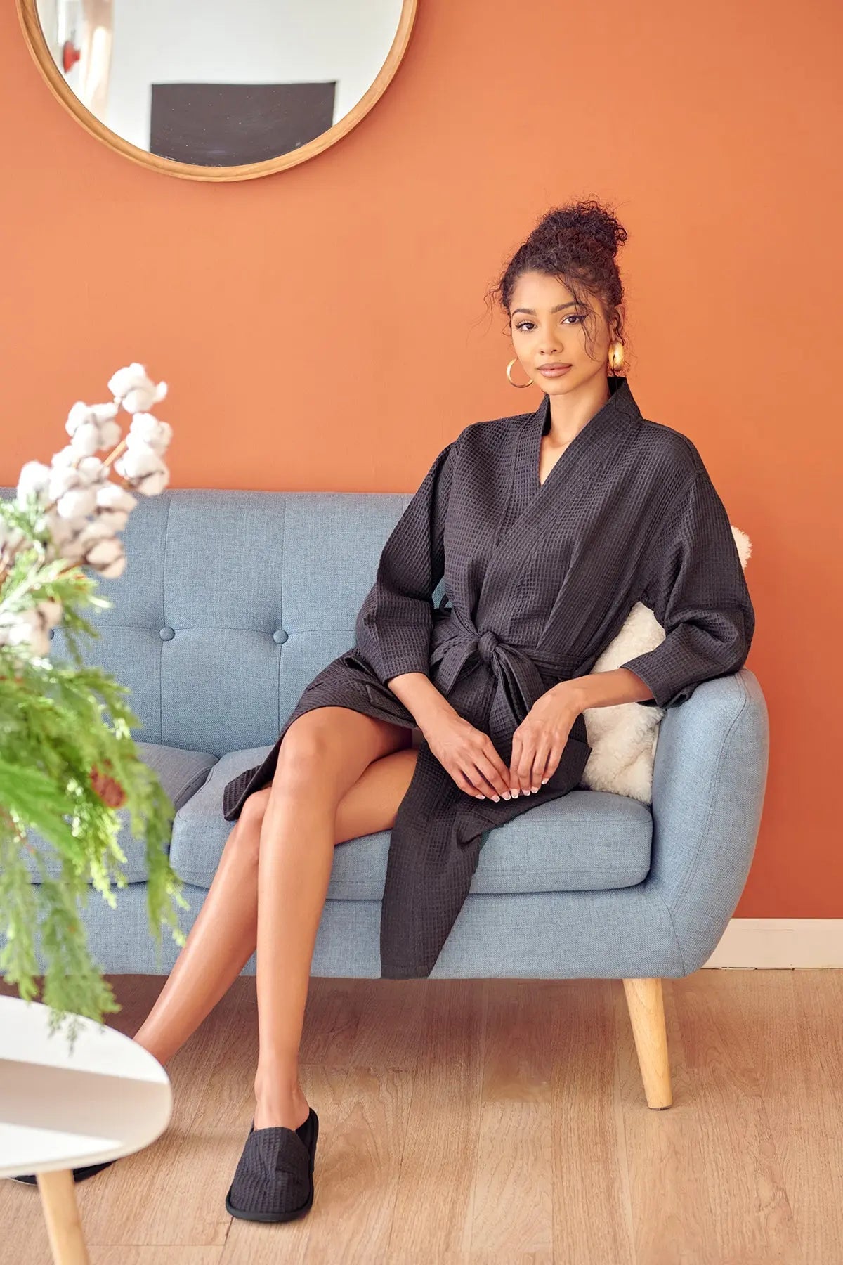 Woman in a dark robe sitting on a light blue sofa against an orange wall.