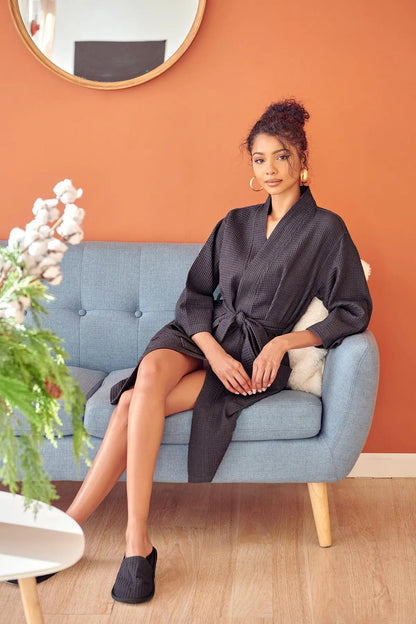 Woman in a dark robe sitting on a light blue sofa against an orange wall.
