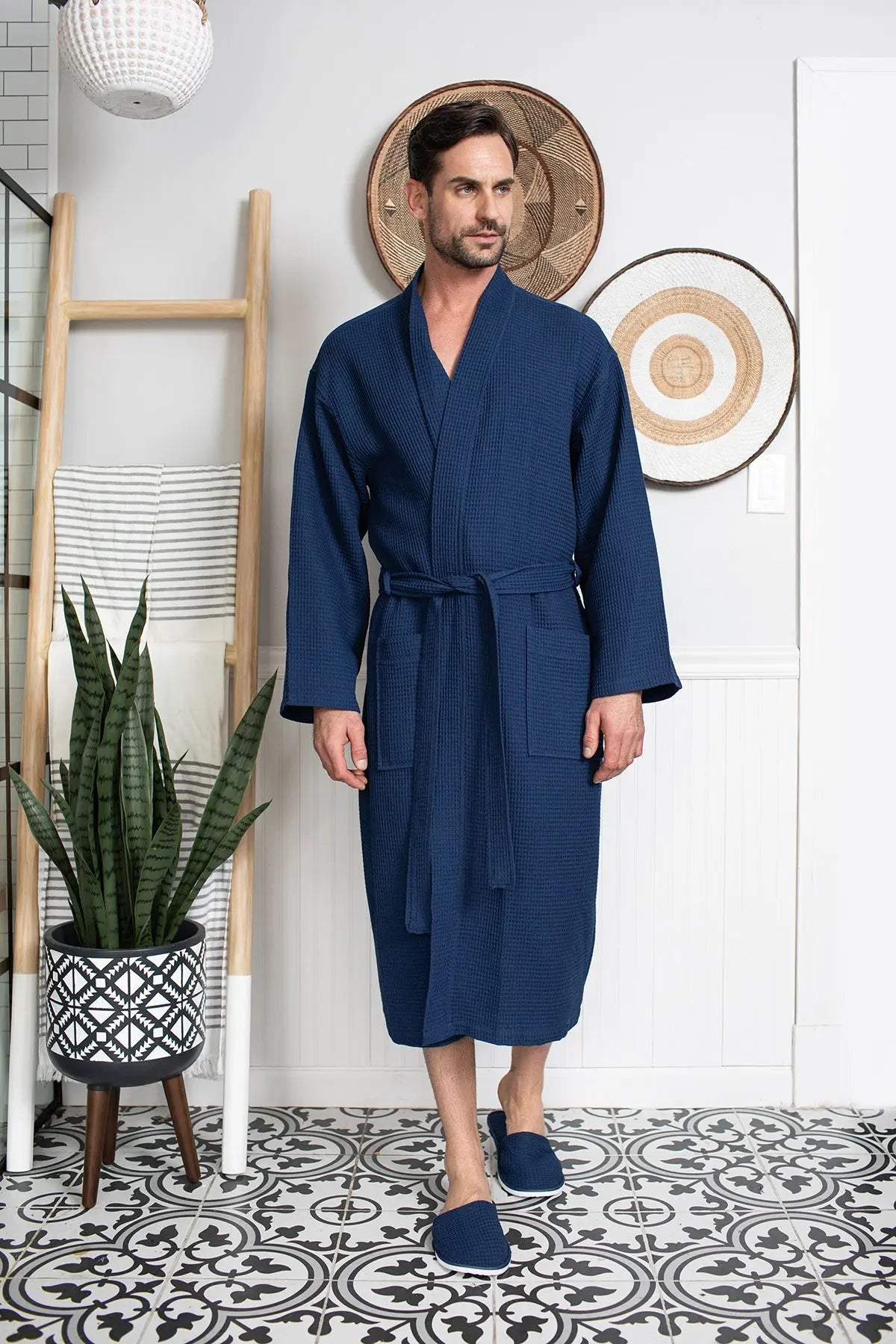 Man wearing a blue robe standing in a room with decorative elements.