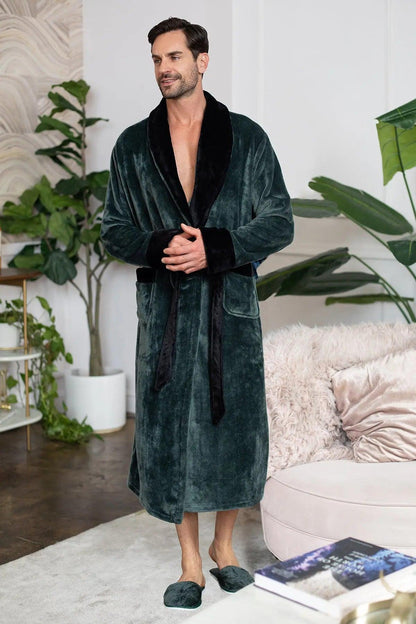 Man wearing a dark green robe in a living room setting with plants and a couch.