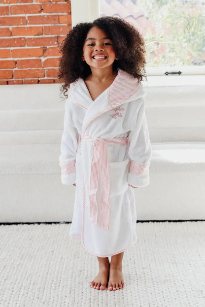 Young girl wearing a white robe with pink accents in a room with a brick wall and window.