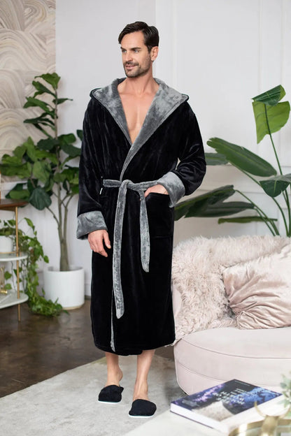 Man wearing a black and gray robe in a living room setting with plants and a couch.