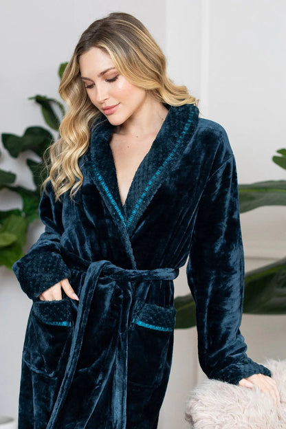 Woman wearing a dark blue robe with a white background and green plants.