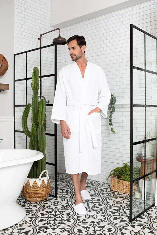Man wearing a white robe in a stylish bathroom with a cactus plant and decorative elements.