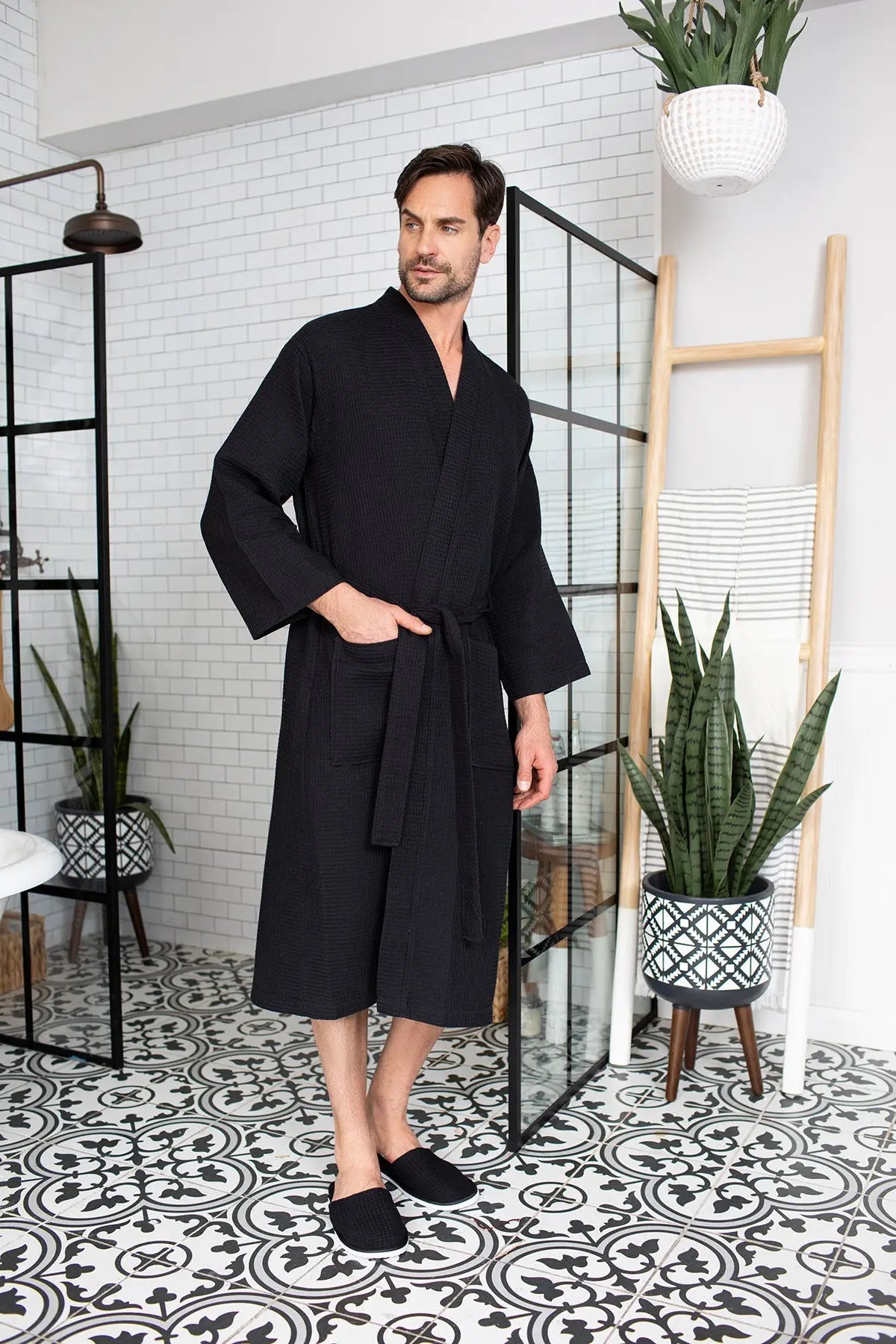 Man wearing a black robe in a stylish room with plants and decor.