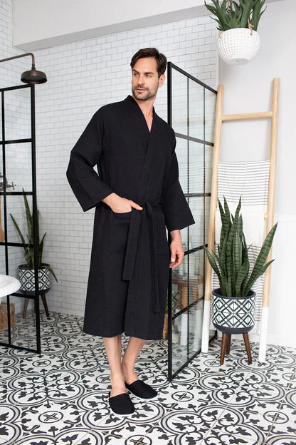 Man wearing a black robe in a stylish room with plants and decor.
