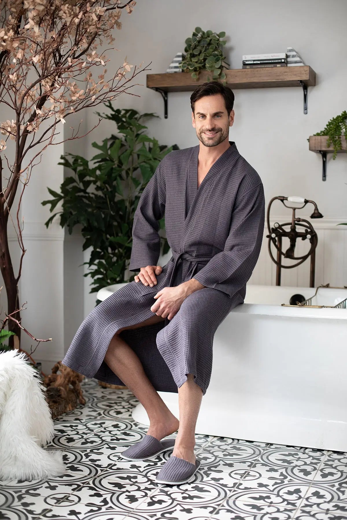 Man in a gray robe sitting by a bathtub in a stylish bathroom.