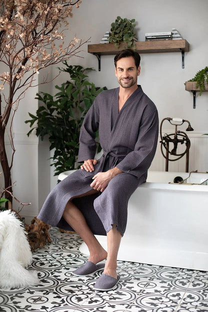 Man in a gray robe sitting by a bathtub in a stylish bathroom.
